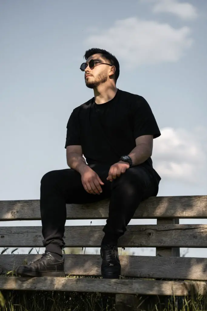homem tatuado usando roupas pretas sentado em um banco